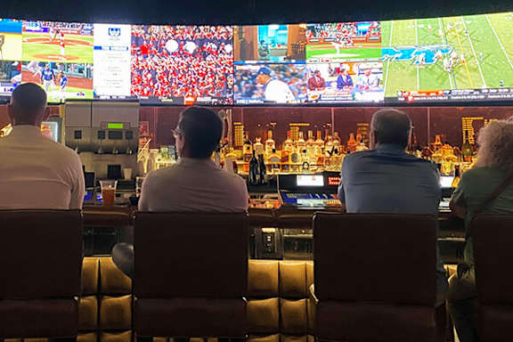 Four people are sitting in front of multiple screens watching a baseball game.