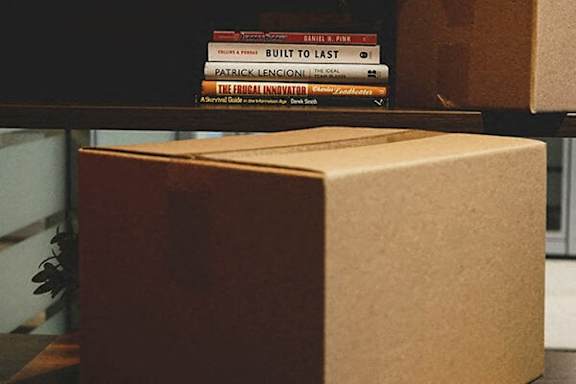 A stack of books on a shelf with a cardboard box in the foreground.