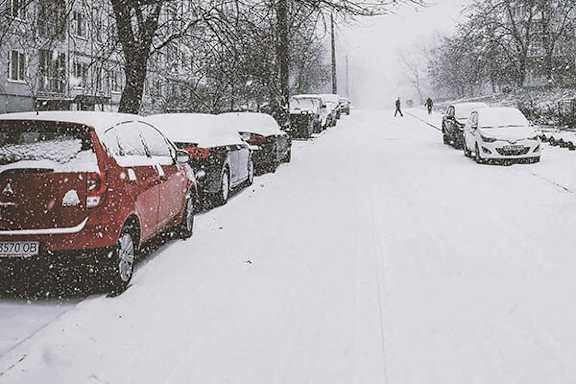 A snowy street with cars parked on both sides.