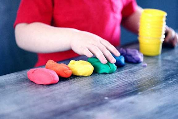 A person is playing with colorful playdough on a table.