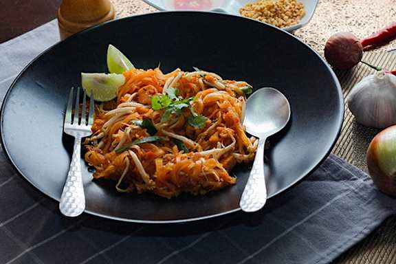 A black plate with a spoon and fork on it with a dish of food on it.