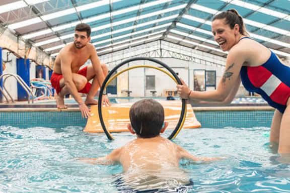 A woman in a red, white and blue swimsuit is teaching a young boy how to swim in a pool.