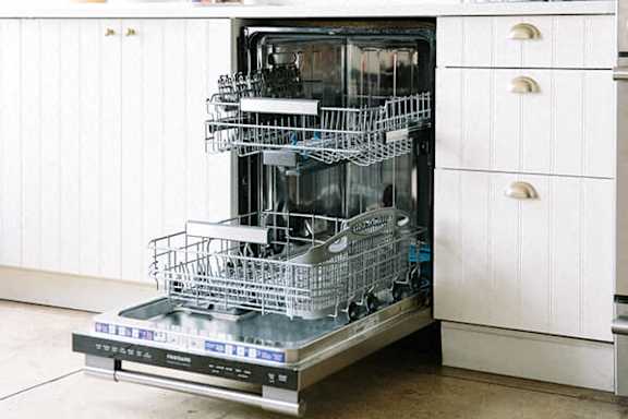 A dishwasher with an open door and several racks of dishes inside.