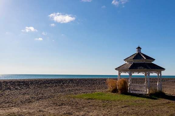 A gazebo sits on a beach with a body of water in the background.