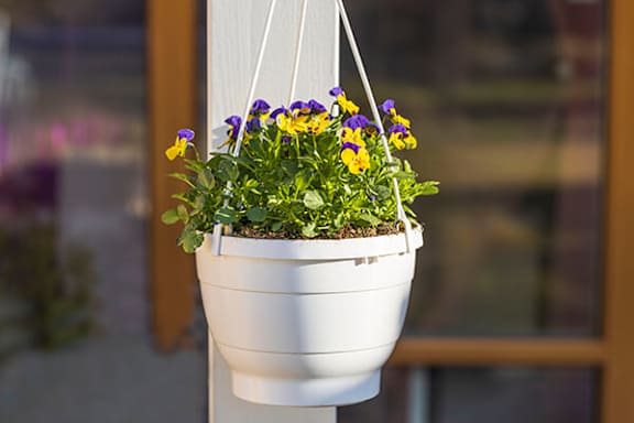 A white hanging planter with purple and yellow flowers.