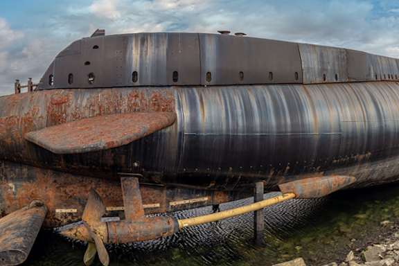 An old, rusted submarine sits on the shore.