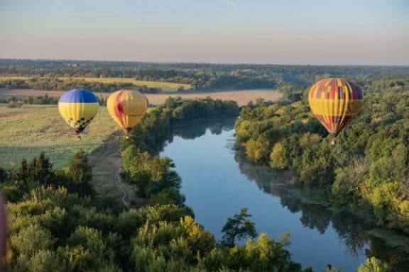 three hot air balloons flying over a river