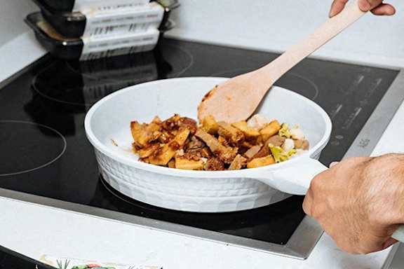 A person is stirring a dish in a white bowl on a stove.