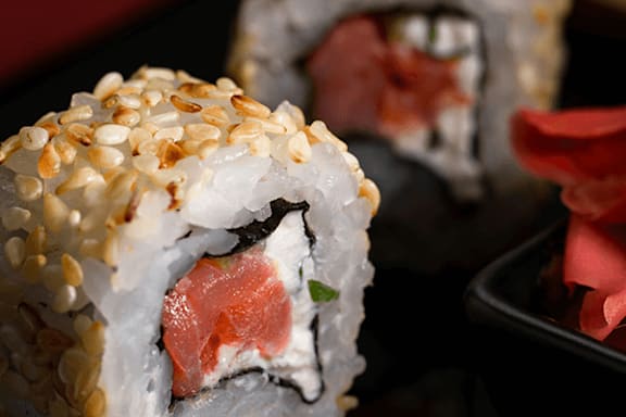 A close up of a sushi roll with sesame seeds on top.