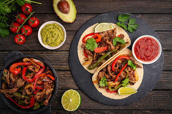 A wooden table with tacos, salsa, and avocado.