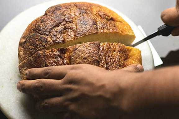 A person cutting a loaf of bread with a knife.