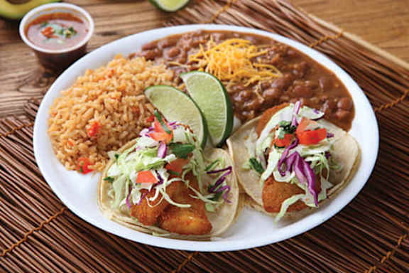 A plate of Mexican food including tacos, rice, beans and tortilla chips.
