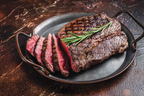 A steak is sliced and laid out on a plate with a sprig of rosemary on top.