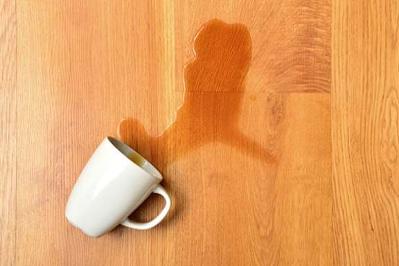 A white cup on a wooden surface with a spill.
