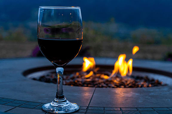 A glass of wine is placed in front of a fire pit.
