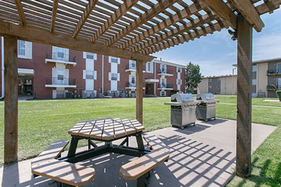 a pergola with a picnic table and two bbq grills in front of