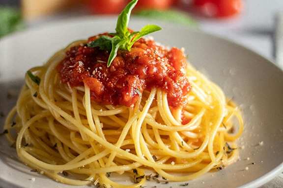 A plate of spaghetti topped with a red sauce and a sprig of basil.