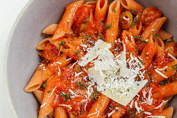 A bowl of pasta with tomato sauce and grated cheese on top.