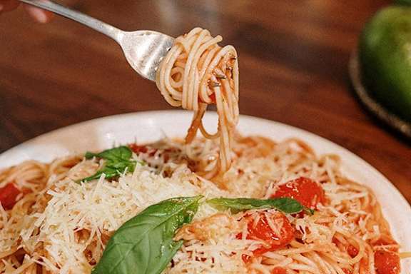 A fork lifting spaghetti from a plate with tomato sauce and basil.
