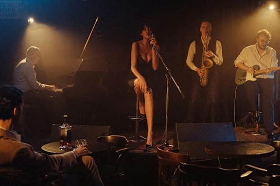 A woman is singing into a microphone while three musicians play instruments behind her.
