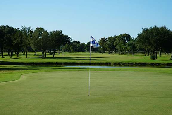 A golf course with a blue and white flag on a pole.