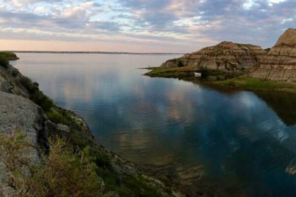 A serene lake surrounded by rocky cliffs and a small house on the shore.