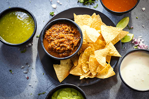 A plate of nachos with guacamole, salsa, and cheese sauce.