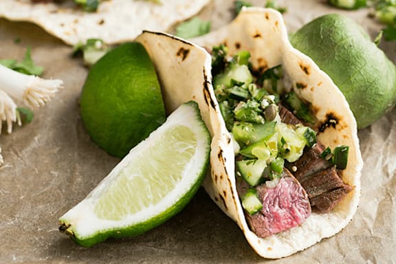 A close up of a taco with meat, cilantro, and lime.