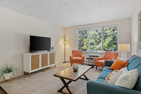 Carpeted living room with large window at Lakecrest Apartments. 