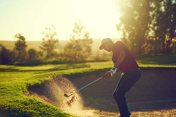 A golfer is seen hitting a ball out of a sand trap.