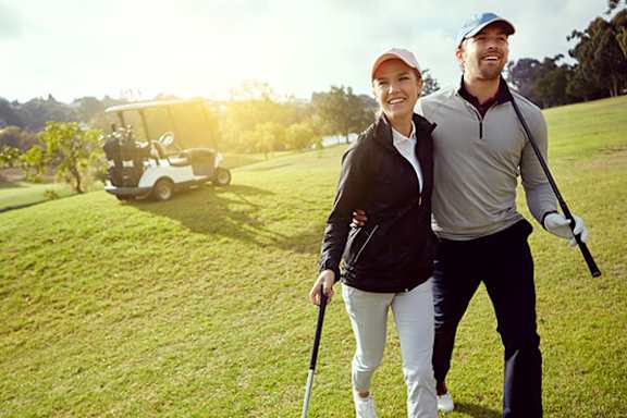 A man and woman stand on a golf course holding golf clubs.