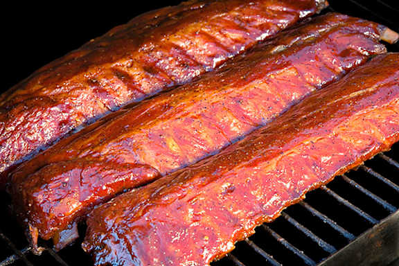 Three slabs of meat are cooking on a grill.