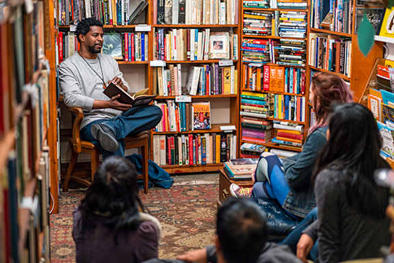 A man is reading a book to a group of people in a library.