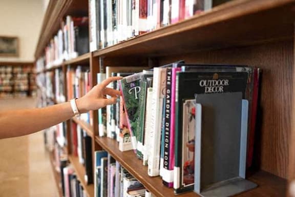 a person reaching for a book on a library shelf