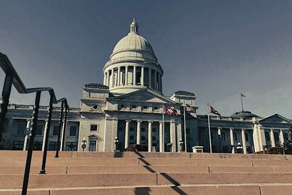 A large, white, domed building with columns and flags in front.