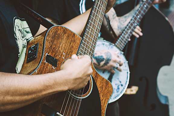 A person is playing a guitar with another person playing a double bass in the background.