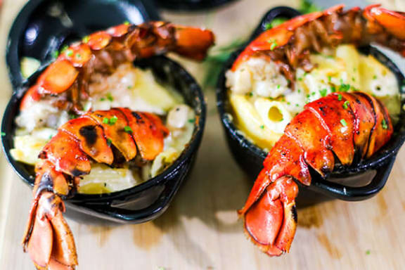 two black bowls filled with mashed potatoes and lobster claws on a wooden table