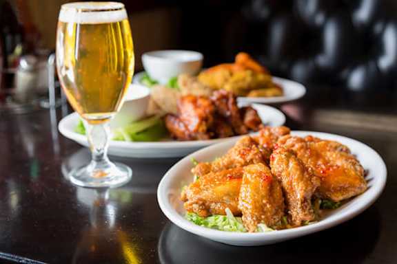 A plate of chicken wings and a glass of beer on a table.