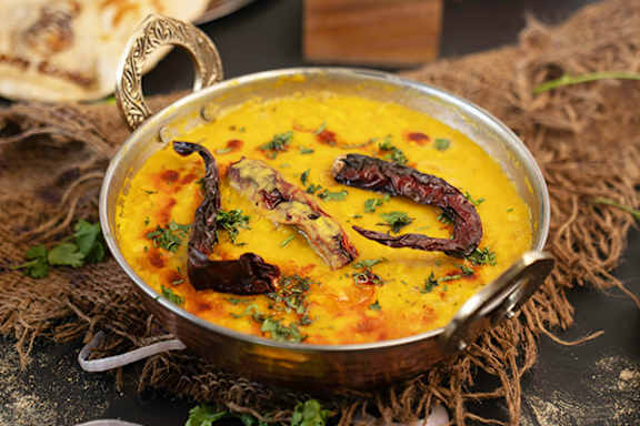 A bowl of yellow lentil soup garnished with dried red chilies and herbs.