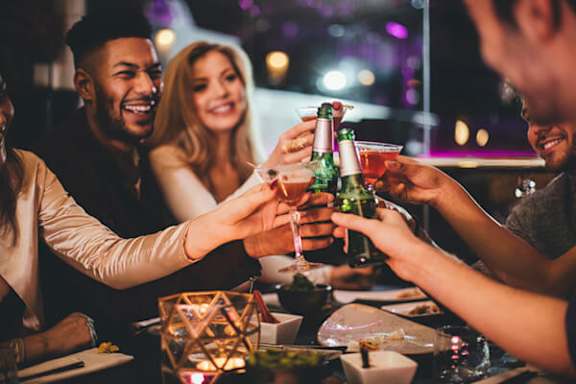 A group of people toasting with drinks at a bar.
