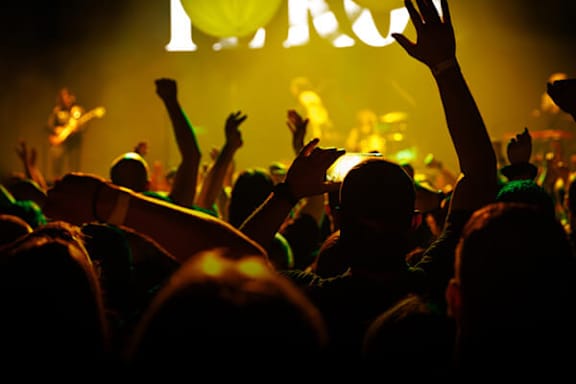 A crowd of people at a concert with their hands raised in the air.