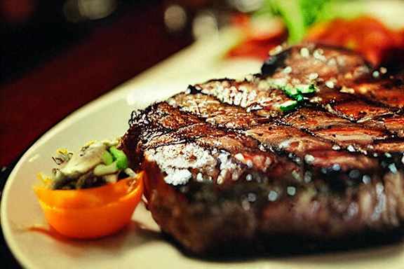 A steak with a garnish of green herbs is served on a white plate.