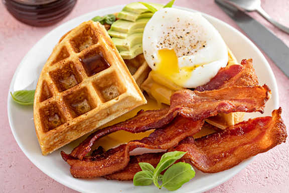 A plate of breakfast food including bacon, egg, and waffle.