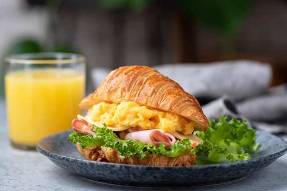 A breakfast sandwich with ham, cheese, and eggs on a croissant.