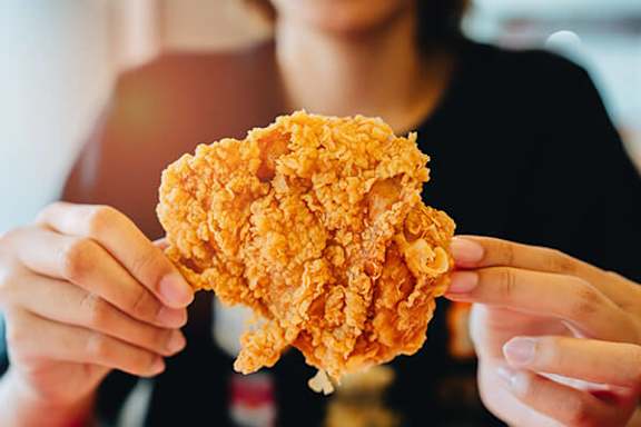 A person holding a piece of fried chicken.