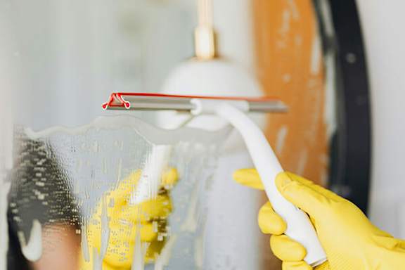 A person wearing yellow gloves is cleaning a window with a squeegee.