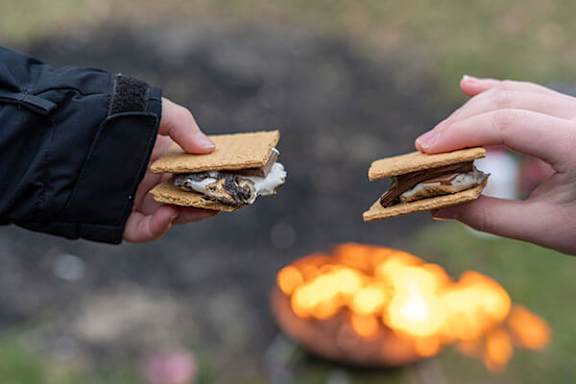 Two hands holding s'mores over a campfire.