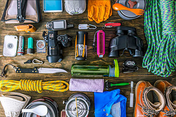 A variety of outdoor equipment is laid out on a wooden surface.