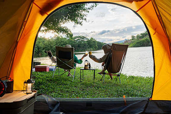 Two people sitting in chairs inside a tent with a lake view.