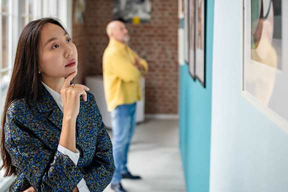 A woman in a patterned jacket is looking at a wall with pictures on it.